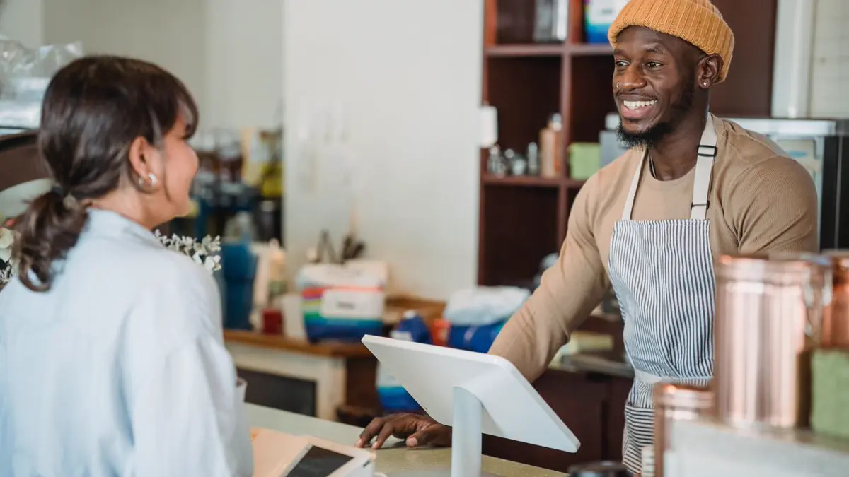 Smiling cafe owner talking with a happy customer at the counter