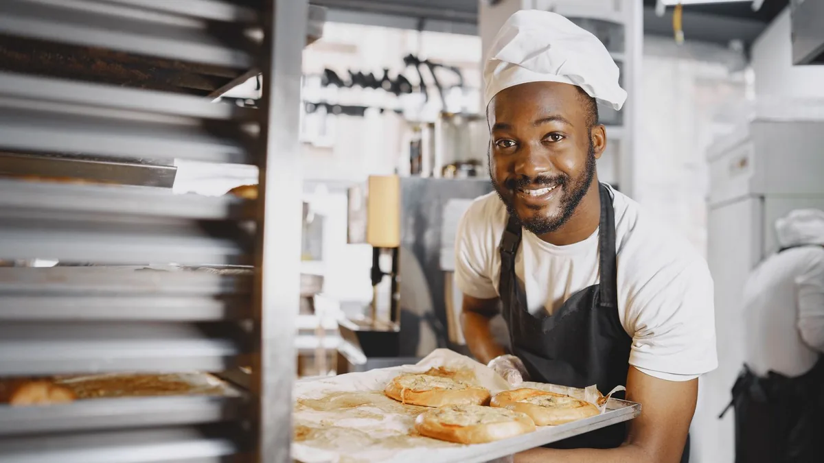Baker holding a tray of fresh bread in a bakery