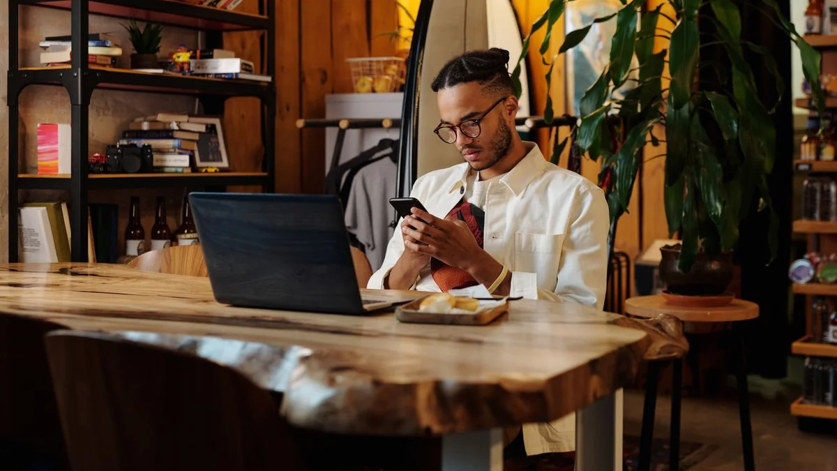 Shop owner using a phone beside a laptop in his shop