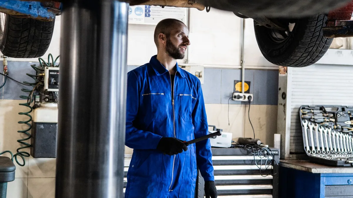 Mechanic in blue overalls standing under a car on a lift in a garage
