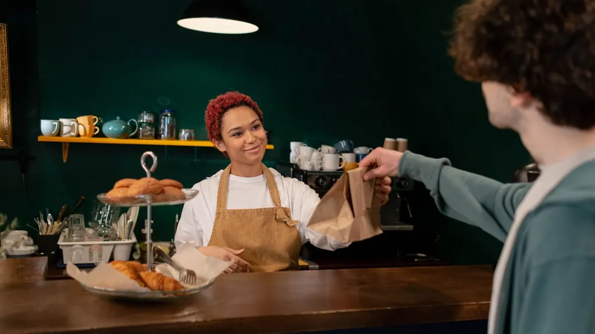 Cafe worker handing an order to a happy customer at the counter