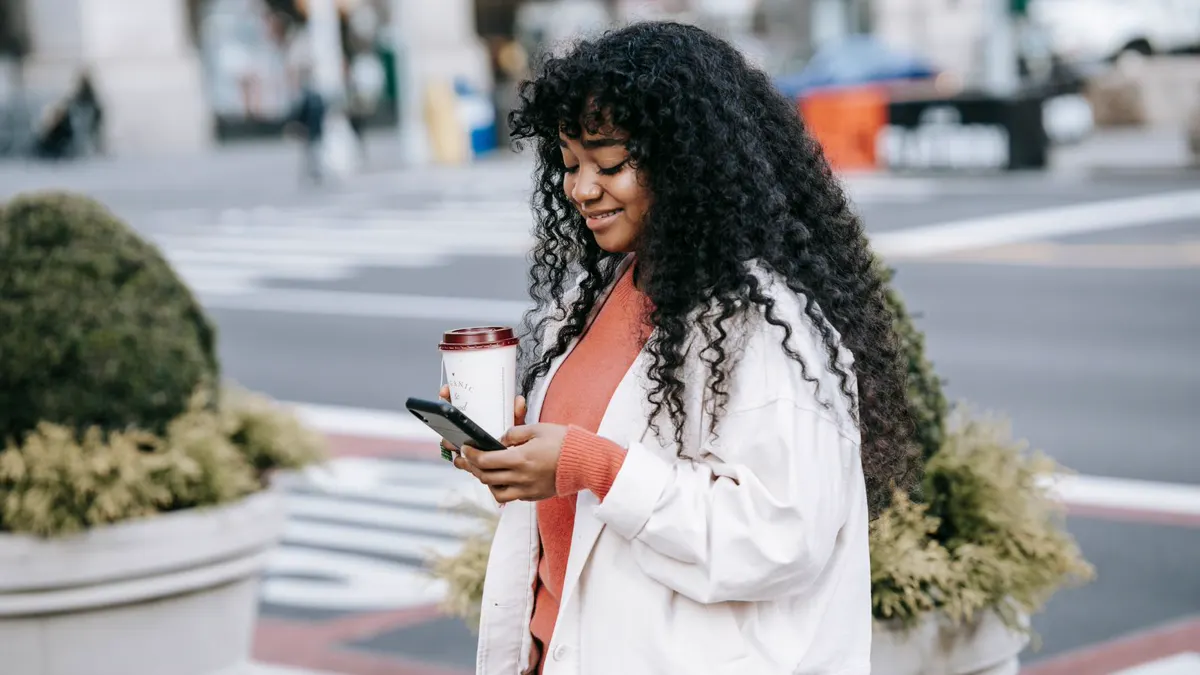 Woman checking her phone on a city street while holding coffee